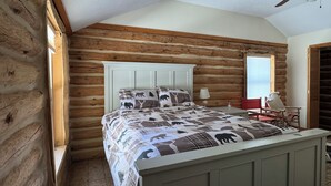 A log cabin bedroom with a bed, a chair, and a window.