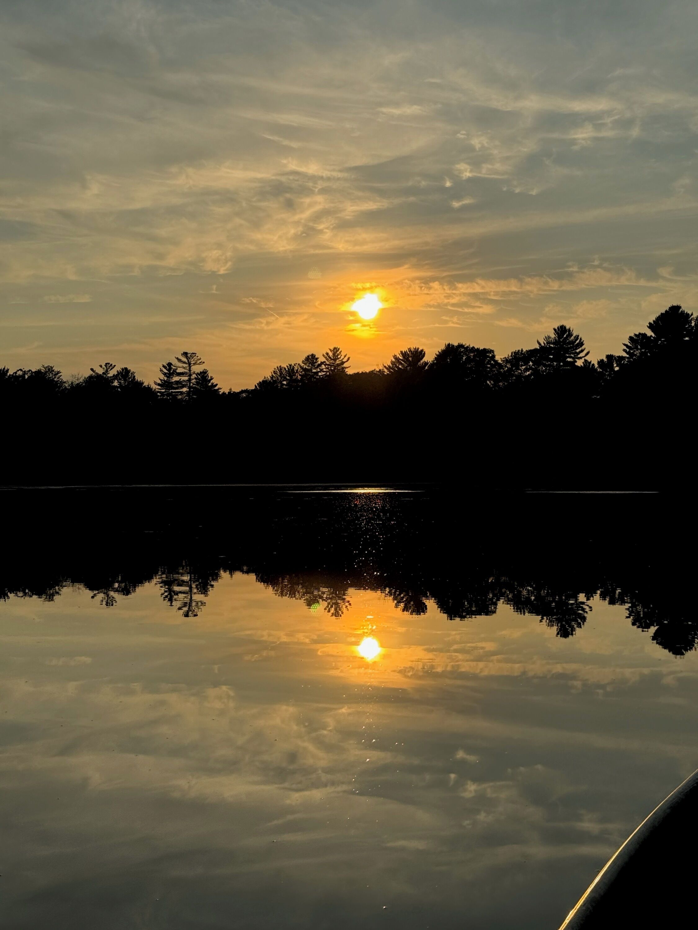 Un lago tranquilo al atardecer, con el sol reflejado en el agua, rodeado de árboles.