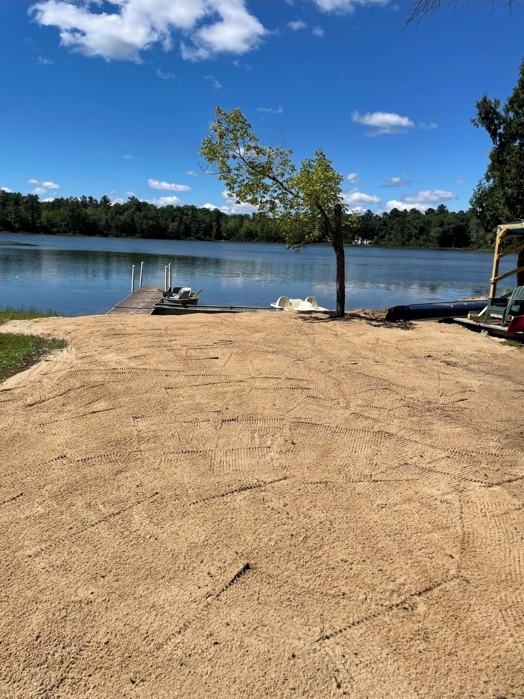 Una zona di spiaggia sabbiosa con un molo e barche, circondata da alberi e un lago.