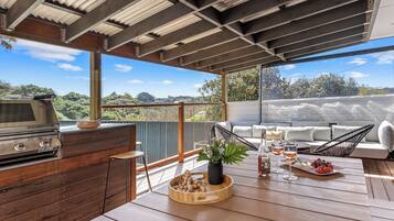 An outdoor patio with a wooden table, a grill, and a seating area with a view of the landscape.