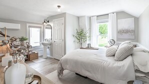 Une chambre à coucher avec un grand lit, une commode, une coiffeuse et une fenêtre avec des rideaux.