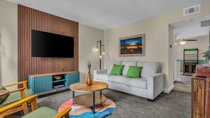 Ein modernes Wohnzimmer mit grauem Sofa, einer Wand aus Holzpaneelen, einem Flachbildfernseher und einem Gemälde.