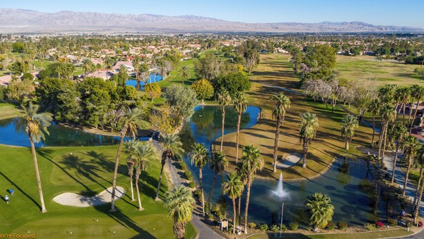Ein Golfplatz mit mehreren Teichen, Palmen und einer Wüstenlandschaft im Hintergrund.
