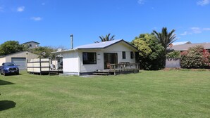 A single-story mobile home with a porch and a small deck, surrounded by a well-maintained lawn and a parked blue truck.