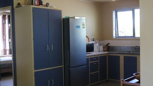 A compact kitchen with dark blue cabinets, a refrigerator, a microwave, and a window with blinds.