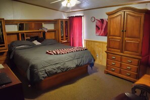 A bedroom with a bed, wooden wardrobe, and a desk with a keyboard.