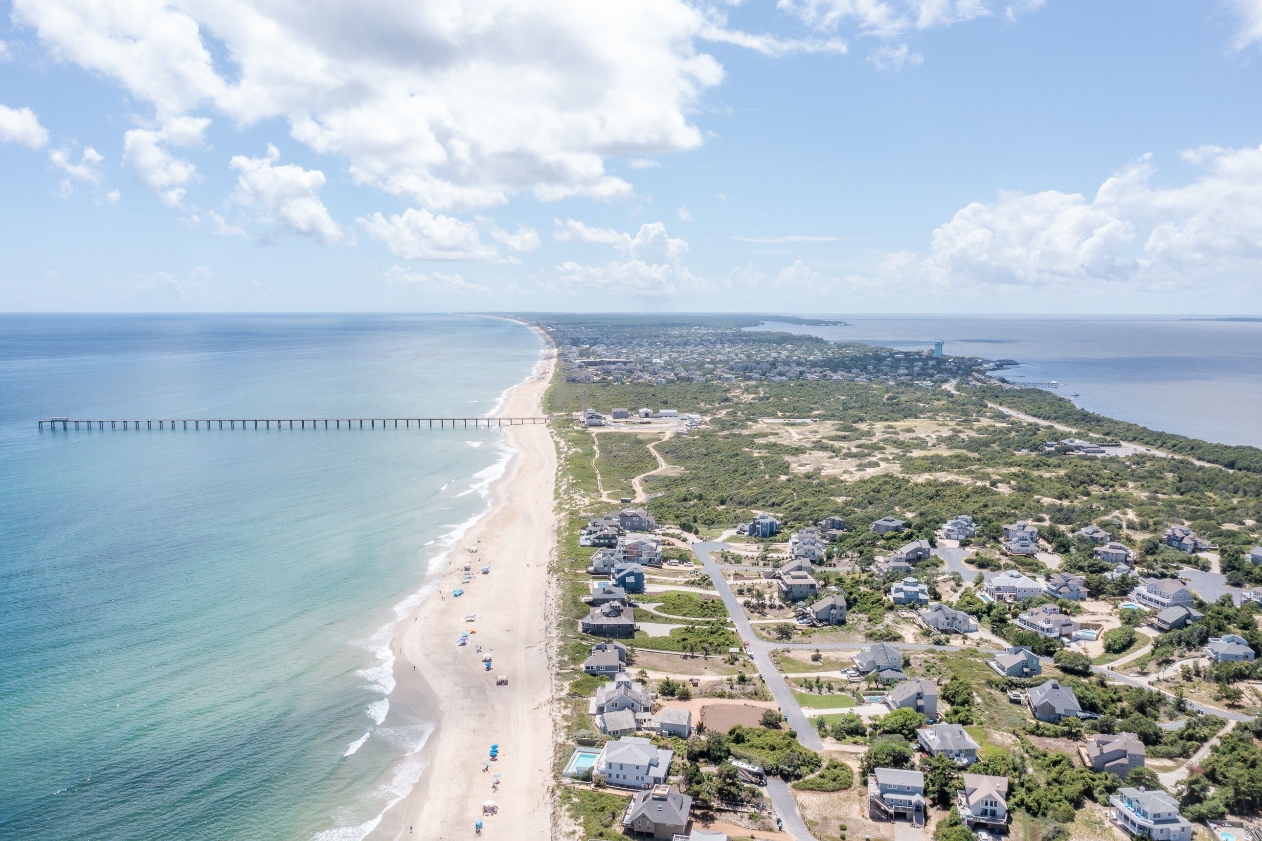 An aerial view of a coastal area with a beach, a pier, and residential buildings.