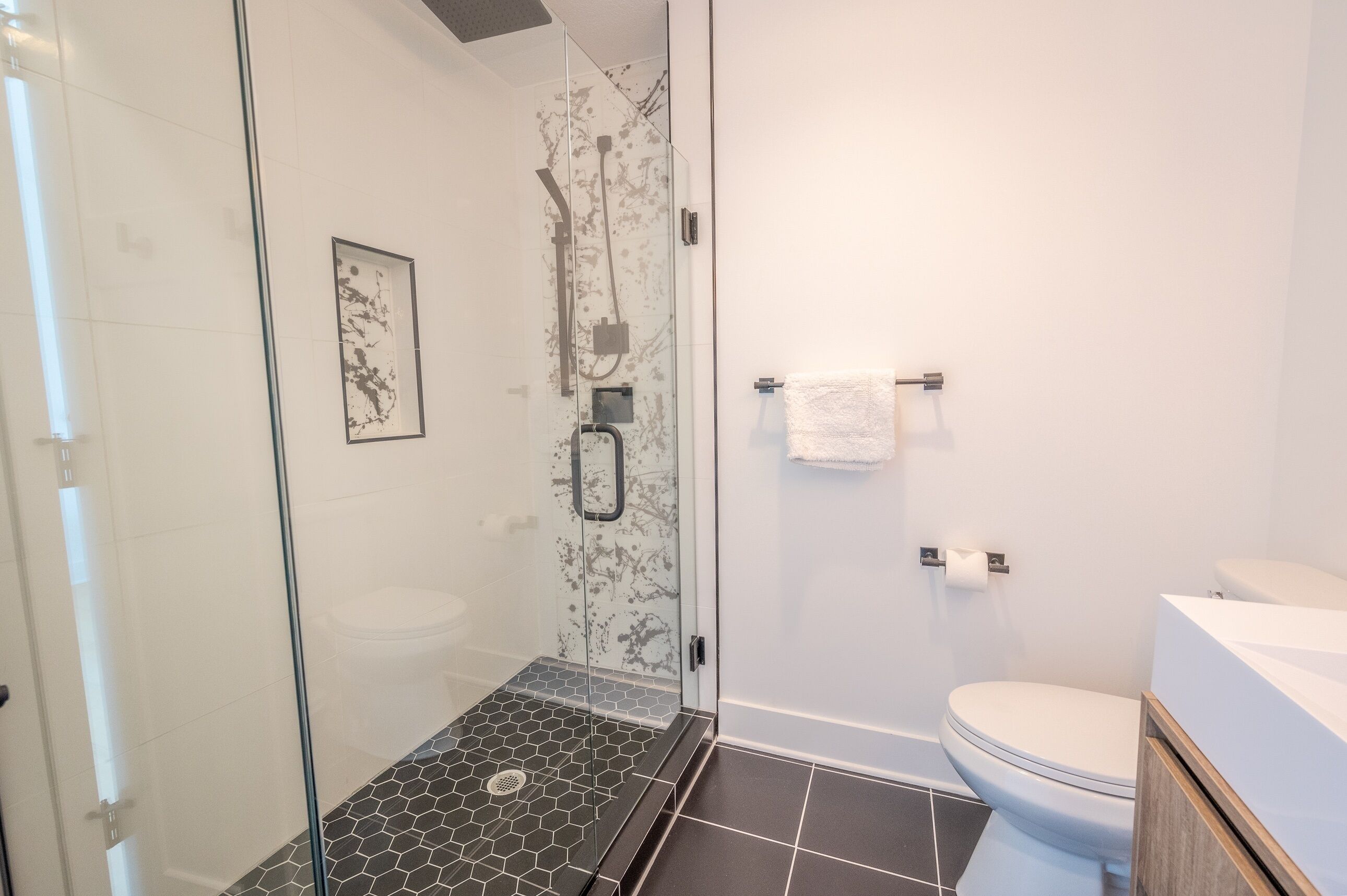 A modern bathroom with a glass-enclosed shower, a toilet, and a sink.