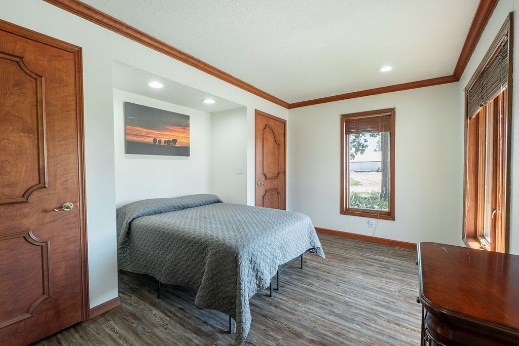 A bedroom with a bed, a wooden door, a window, and a picture on the wall.