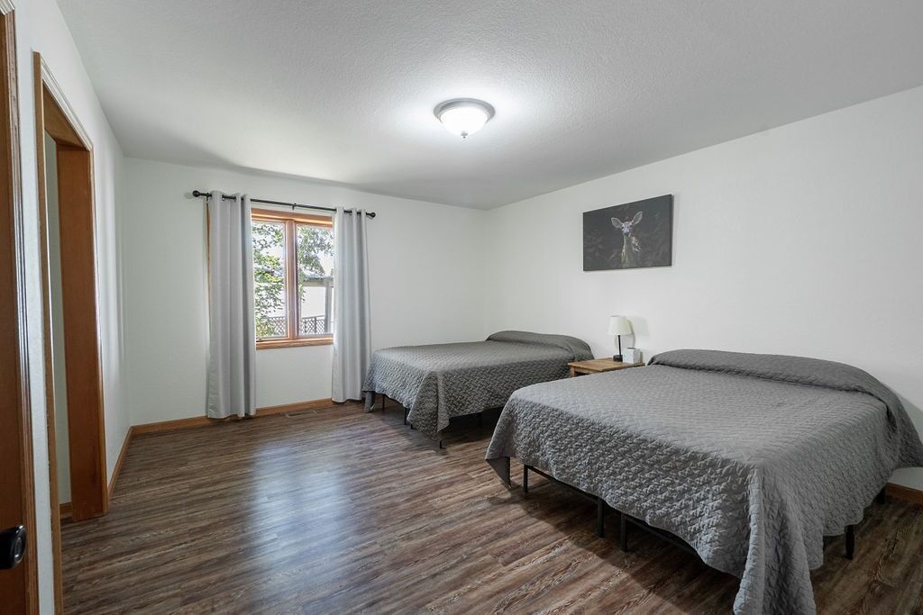 A room with two single beds, a window with curtains, a ceiling light, and a wall-mounted artwork.