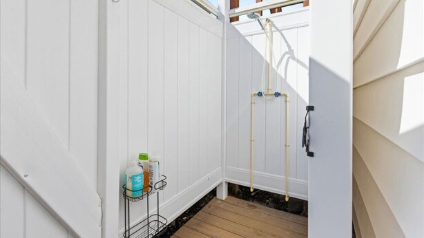 A small, enclosed outdoor space with a wooden deck, white walls, and a metal rack holding cleaning supplies. - 4BR Home w/ Rooftop Deck - 3 Block to Beach (Ventnor City)