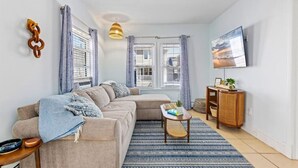 A living room with a sofa, a coffee table, a TV, and a window with curtains. - 4BR Home w/ Rooftop Deck - 3 Block to Beach (Ventnor City)