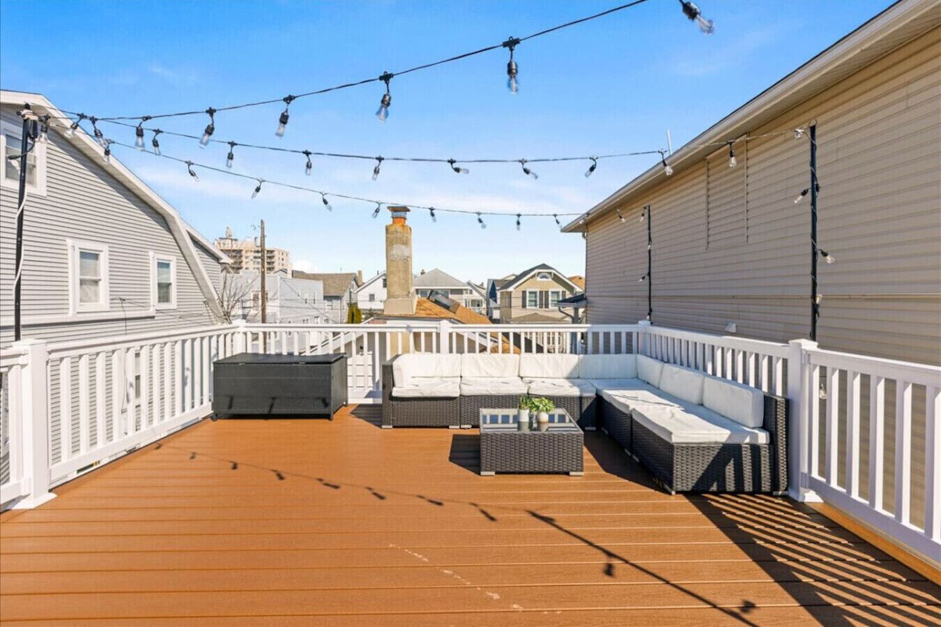 A rooftop deck with a white railing, a gray sofa, and a small table.