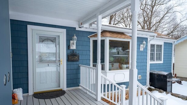 Une maison bleue avec un porche blanc, une pancarte indiquant «Bienvenue» et une boîte aux lettres.