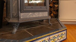 Un poêle à bois traditionnel, orné de sculptures complexes, doté d’un socle décoratif en carreaux et placé devant un mur en pierre.