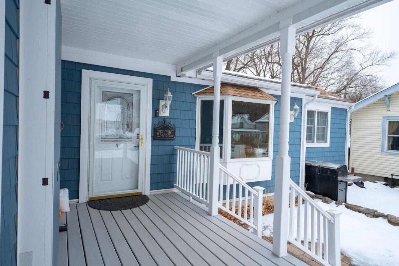 A porch with a white railing, a welcome sign, and a door with a glass panel.