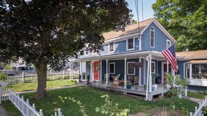 A two-story house with a porch, a flag, and a fenced yard.