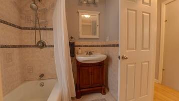 A bathroom with a bathtub, shower, sink, and a door.