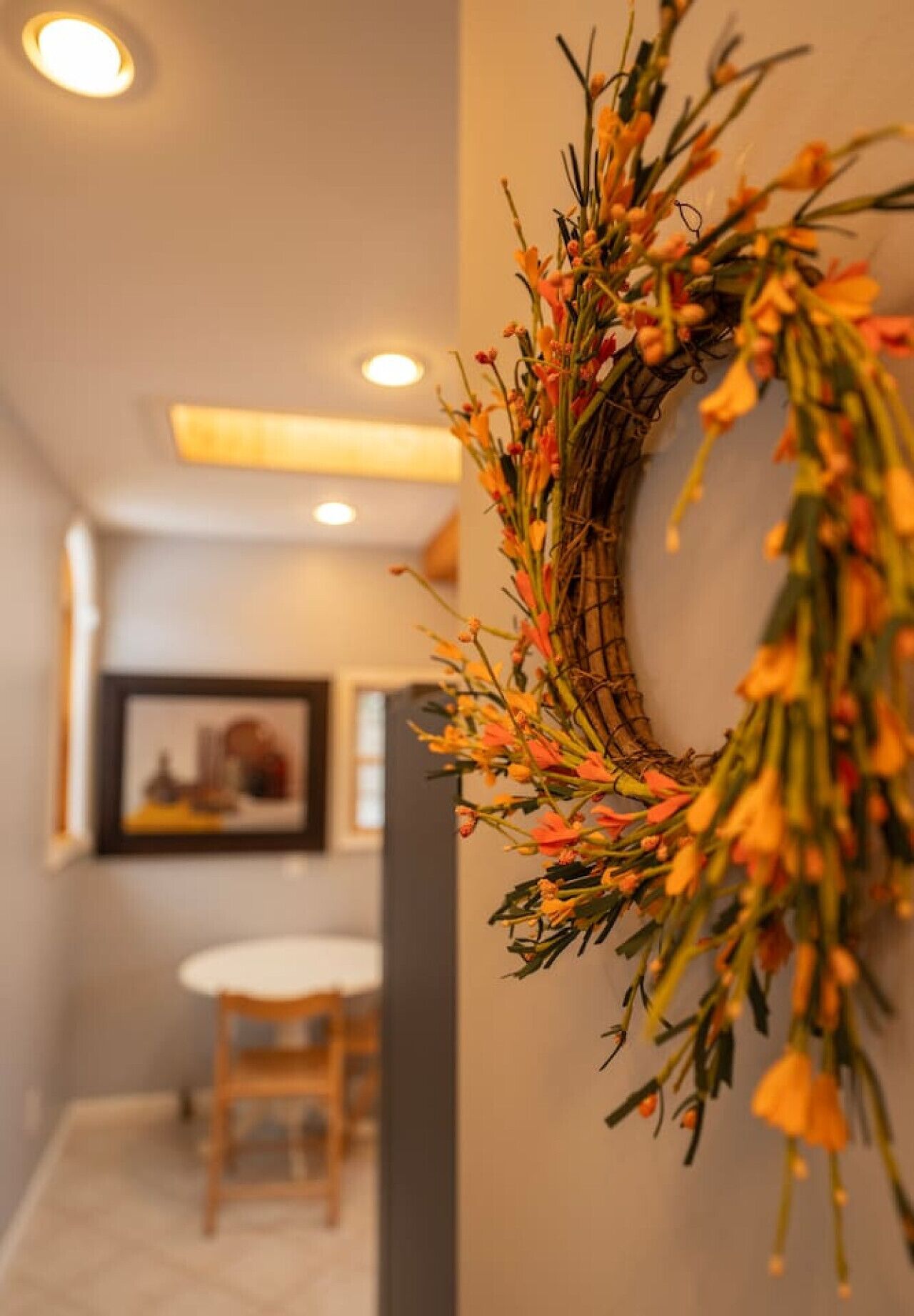 A hallway with a decorative wreath on the wall, a framed picture, and a table with chairs.