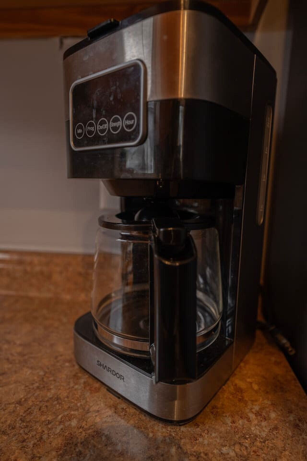 Une cafetière en acier inoxydable dotée d’un panneau de commande numérique et d’une verseuse transparente.