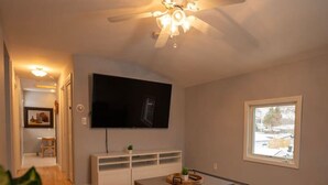 A living room with a ceiling fan, a flat-screen TV, a coffee table, a sofa, and a window with a view.