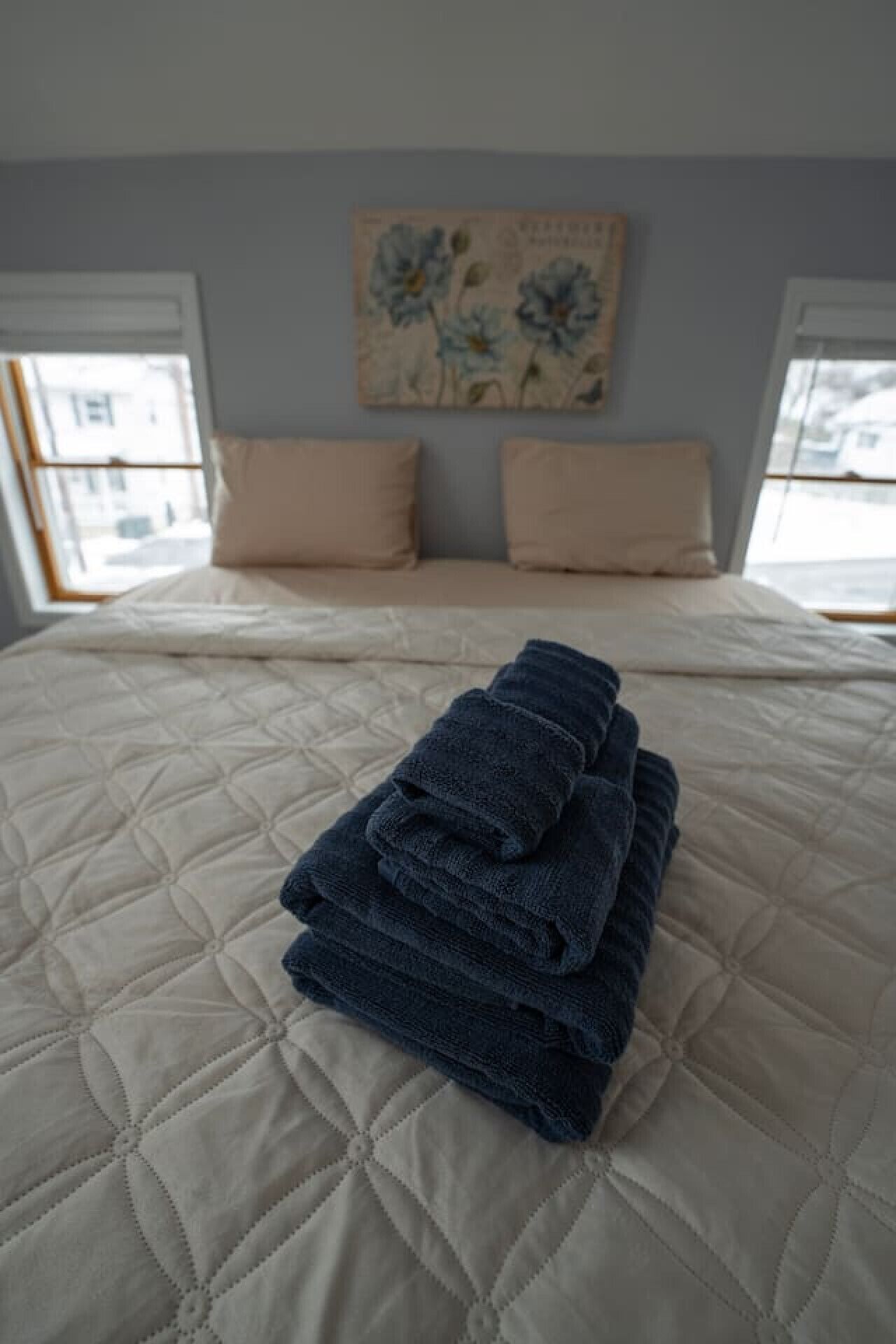 A bed with a quilted cover, two pillows, and a stack of folded towels.