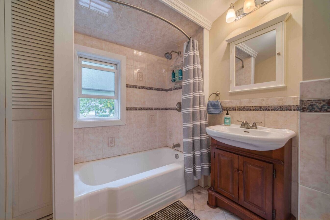 Ein Badezimmer mit Badewanne, Fenster, Duschvorhang, Waschbecken und Spiegel.