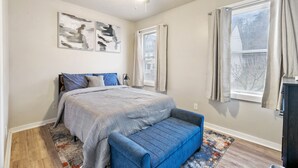 Een slaapkamer met een bed, een blauwe bank, een plafondventilator en kunst aan de muur.