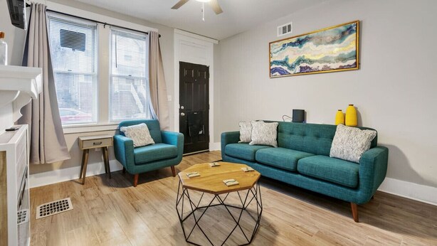 Una sala de estar con un sofá color turquesa, un sillón azul, una mesa de centro de madera y un ventilador de techo.