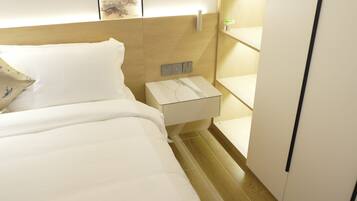 A hotel room with a bed, a nightstand, a wall-mounted light, and a shelf.