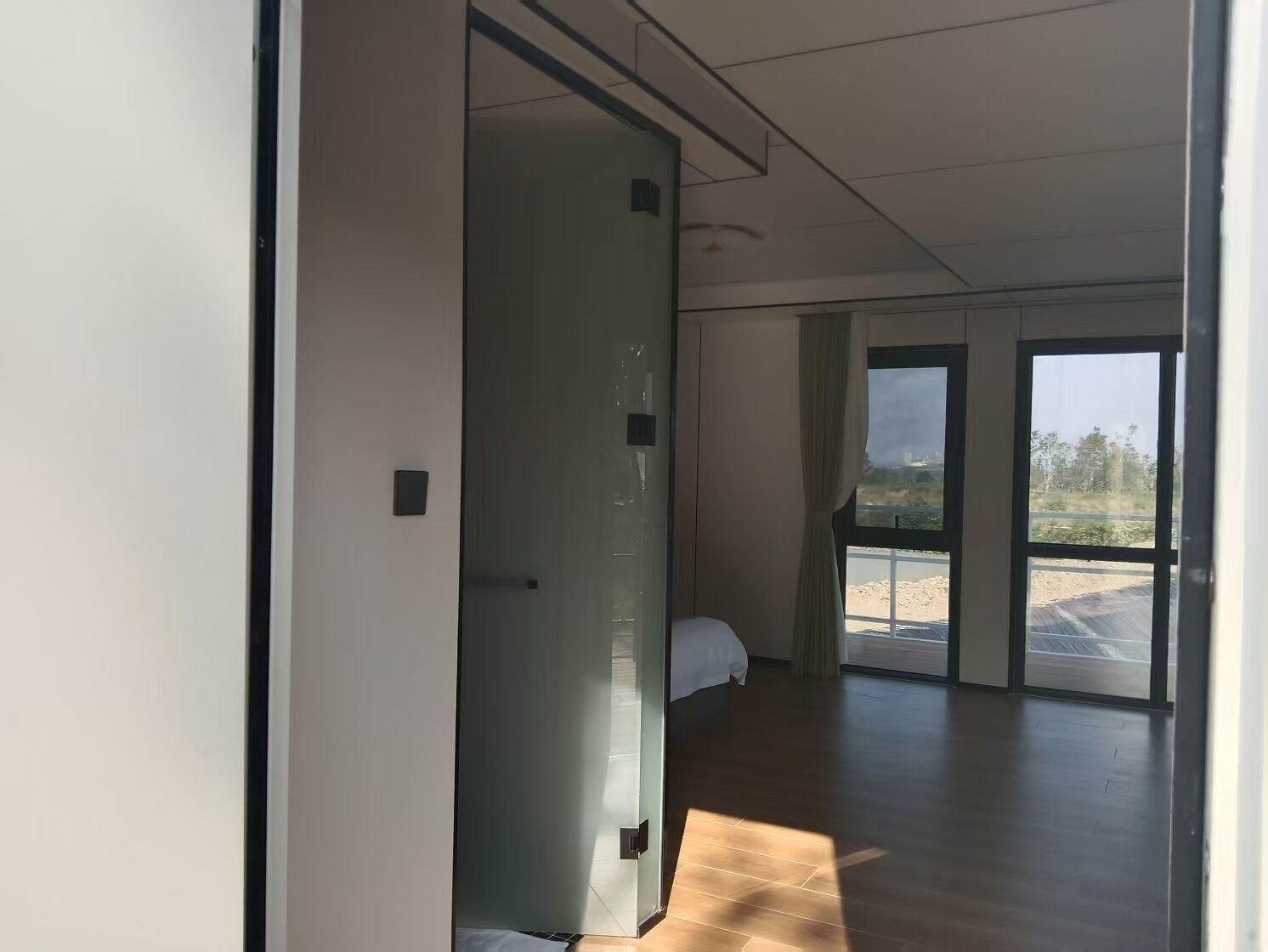 A modern hotel room with a large sliding door leading to a balcony, a bed, and a view of the outdoors.