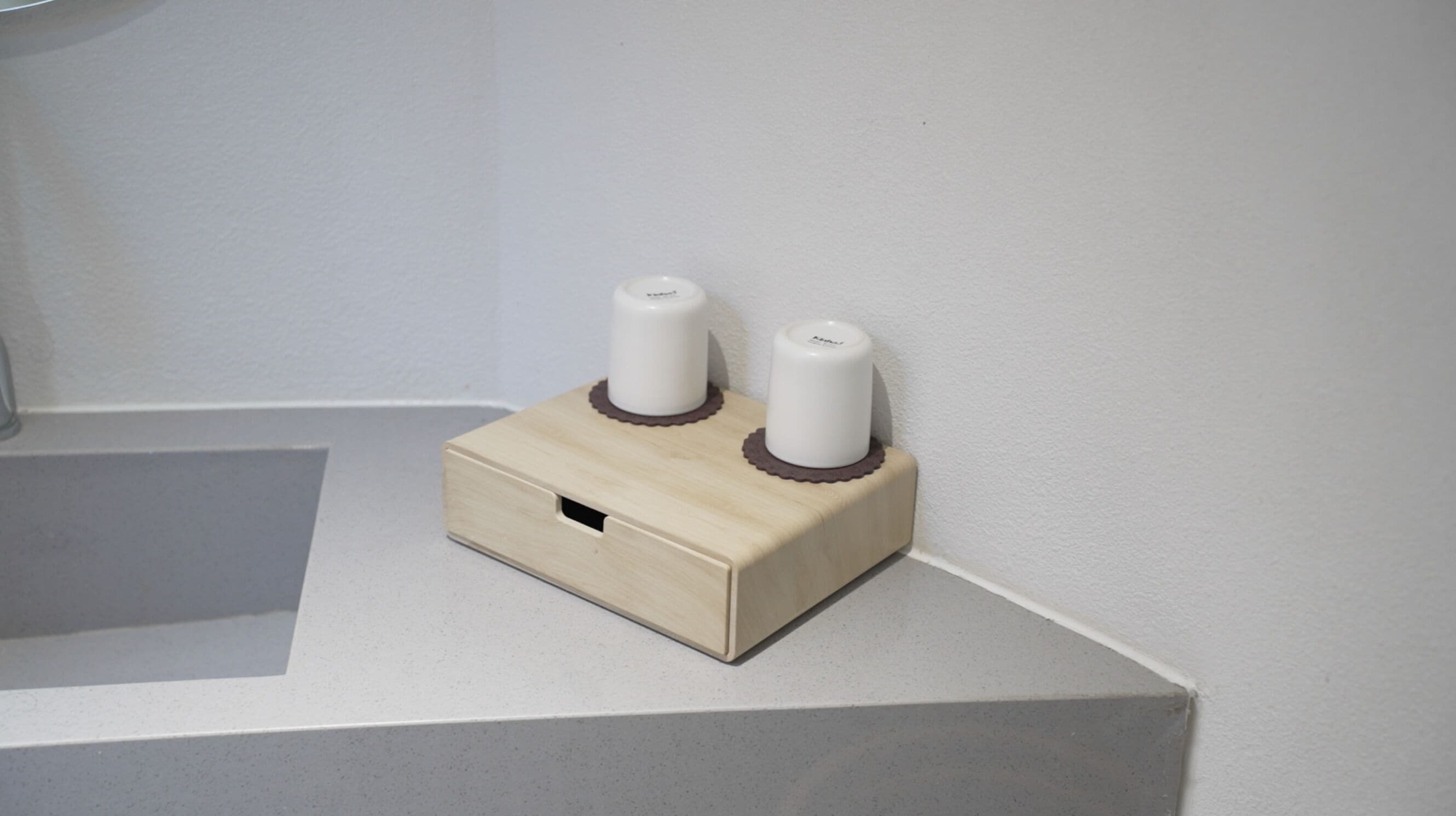 Un objeto de madera con dos elementos cilíndricos blancos encima, sobre una superficie blanca frente a una pared blanca.