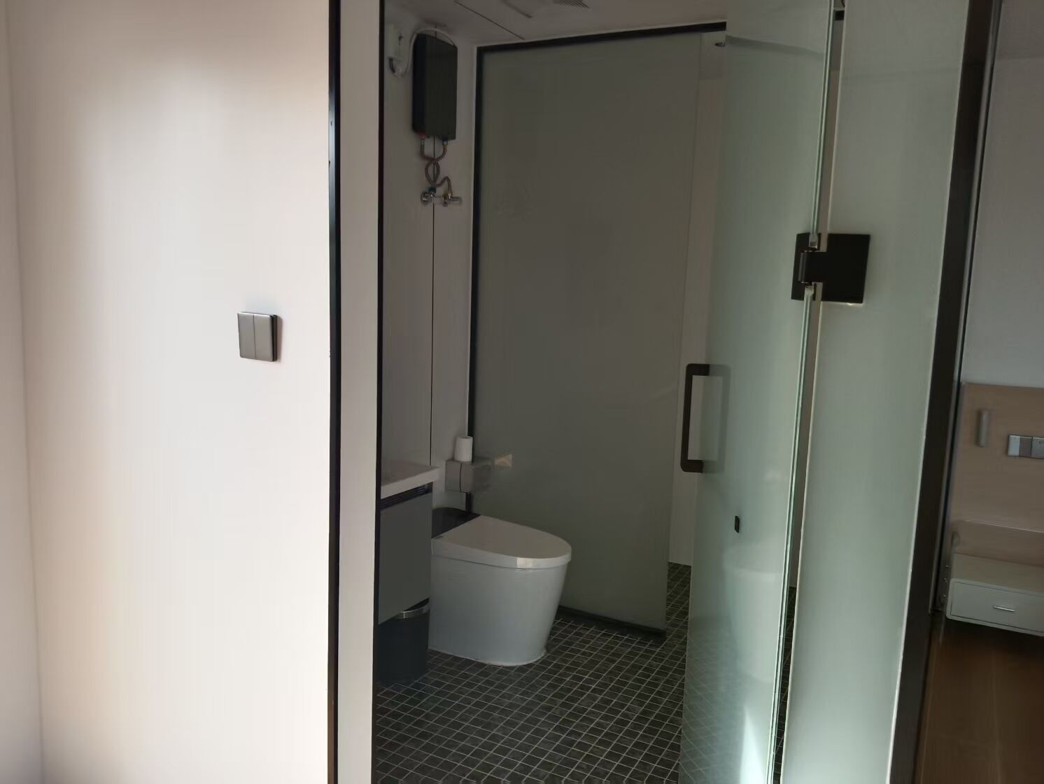Un baño moderno con inodoro, cabina de ducha de vidrio y lavamanos blanco.