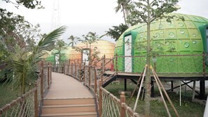 A pathway leading to spherical structures with a green exterior and a white door, surrounded by greenery and a wooden fence. - Unicorn Rocket Resort (Wenchang)