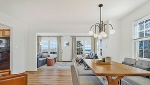 A modern living room with a wooden dining table, a sofa, and a large window with a view. - Kick back and enjoy the Chesapeake & this 3-bedroom, relaxing, stylish space. (Prince Frederick)