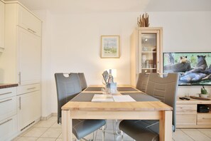 Un coin repas comprenant une table en bois, des chaises noires, un téléviseur et un meuble avec des portes en verre.