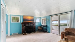A room with a fireplace, a laptop on a table, a couch, and a view through a sliding glass door. - Cozy Lake house in Hilton with beach access. (Hilton)