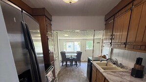 A kitchen with wooden cabinets, a stainless steel refrigerator, a marble countertop, and a dining area with a table and chairs. - Cozy Lake house in Hilton with beach access. (Hilton)
