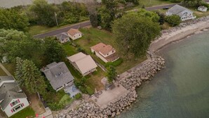 An aerial view of a coastal residential area with houses, a rocky shoreline, and a road. - Cozy Lake house in Hilton with beach access. (Hilton)
