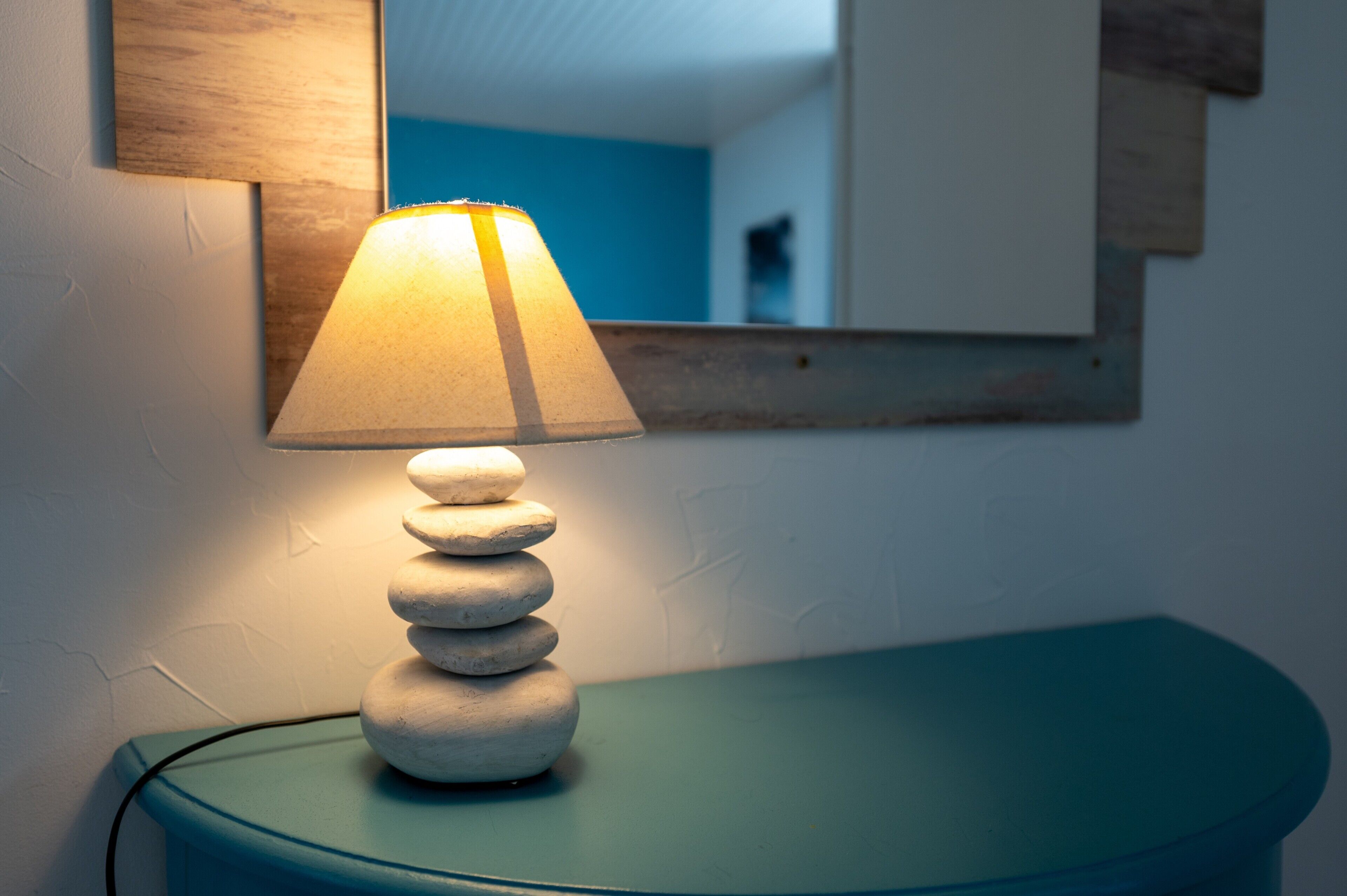 A lamp with a conical shade on a round table, a mirror on the wall, and a blue wall in the background.