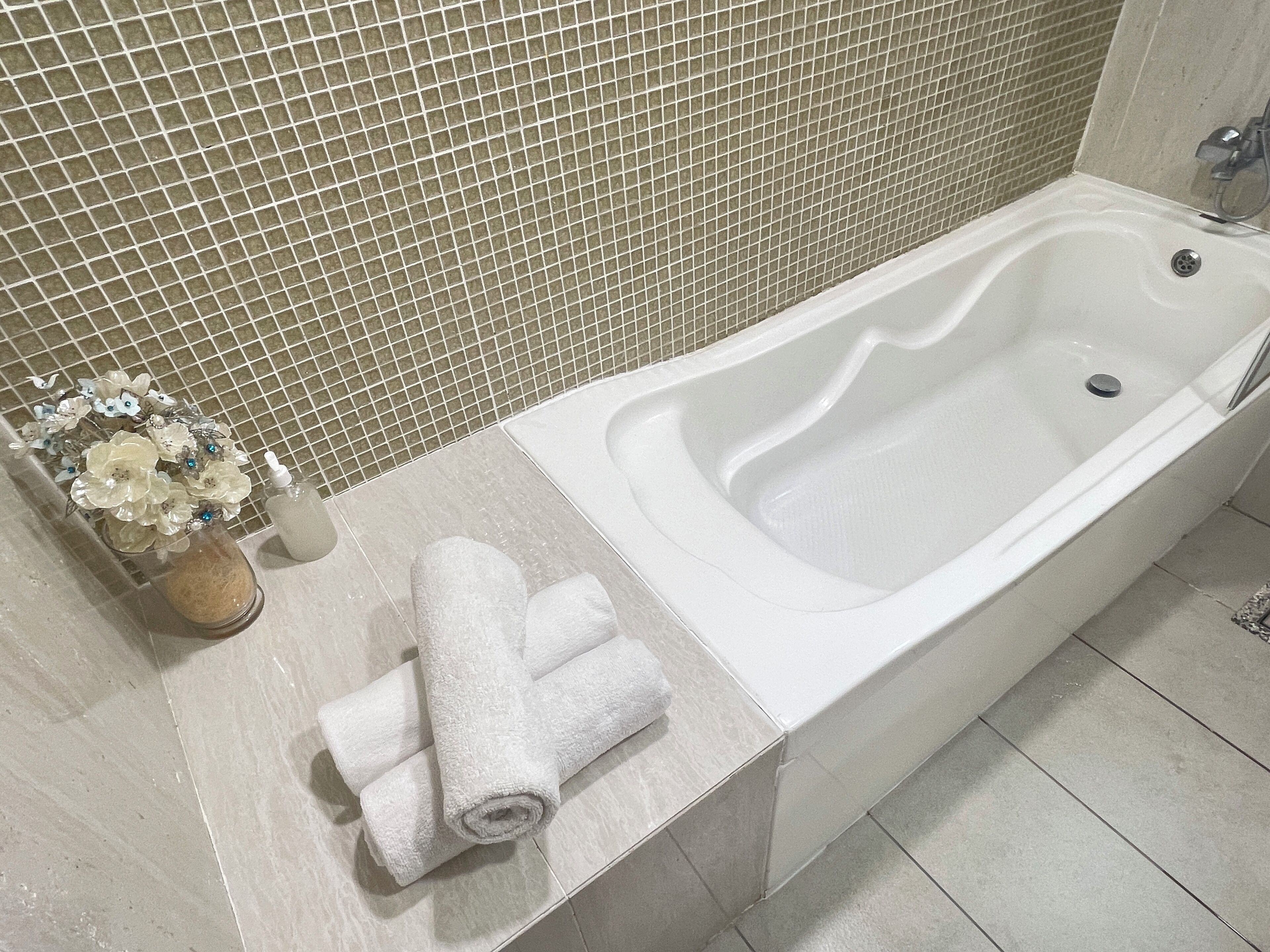 A bathroom with a white bathtub, a tiled wall, and a small vase with flowers on the counter.