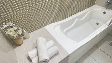 A bathroom with a white bathtub, a tiled wall, and a small vase with flowers on the counter.