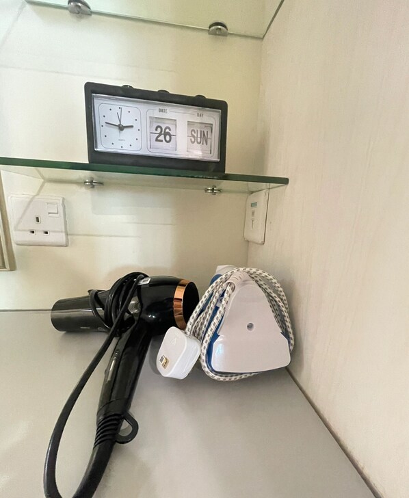 A bathroom with a glass shelf holding a digital clock displaying the date and day, a hairdryer, and a bag with a braided strap. - Riverson soho kota minabalu near imago (Kota Kinabalu)