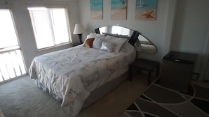 Une chambre avec un grand lit, une table de chevet, une lampe et une fenêtre. Il y a trois tableaux accrochés au mur.