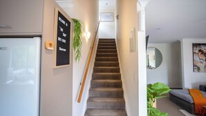 A staircase leading to a landing with a signboard, a refrigerator, a plant, and a sofa in the adjacent room.