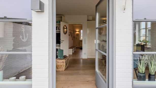A modern interior with a wooden floor, a glass door leading to a hallway, and a white brick wall. - House Dünenwall, App. 1 - Part of the house near the beach with approx. 80 m² and 3 rooms, for (Wenningstedt-Braderup (Sylt))