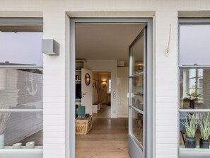 Un intérieur moderne avec un plancher en bois, une porte en verre donnant sur un couloir et un mur en briques blanches.
