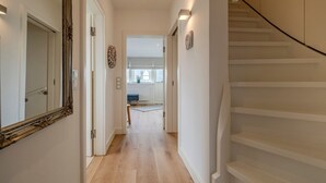 A modern hallway with a wooden floor, a white staircase, and a mirror on the left. - House Dünenwall, App. 1 - Part of the house near the beach with approx. 80 m² and 3 rooms, for (Wenningstedt-Braderup (Sylt))