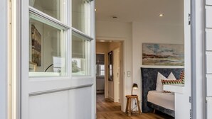 A modern interior with a wooden floor, a sofa with cushions, a lamp on a small table, and a painting on the wall. - House Dünenwall, App. 1 - Part of the house near the beach with approx. 80 m² and 3 rooms, for (Wenningstedt-Braderup (Sylt))