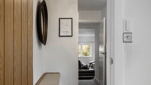 Un pasillo con suelo de madera, pared blanca, un mapa enmarcado, una puerta y una ventana.